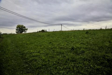 Grassy path on a slope in a field with over head cables on a cloudy day in th Stock Photos
