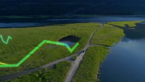 Grassy peninsula hosting forked dirt road SUV kicking dust by water, neon green Stock Footage 332505079