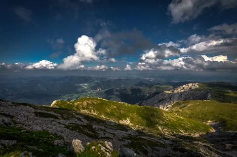 Grassy rax plateau with big patch of shade and dramatic, cloudy, dark blue sky Stock Photos