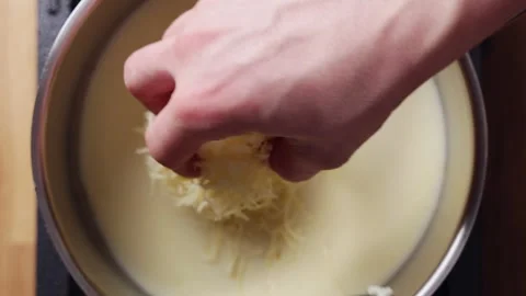 Grated cheese drops into white sauce in saucepan. Stock Footage 341615700