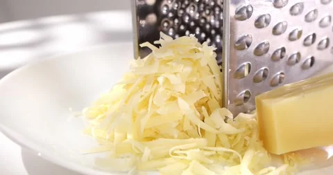 Grated cheese with a grater on a white plate. a piece of hard cheese. Stock Footage 242490889
