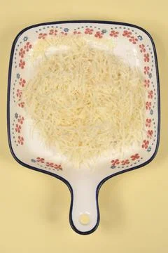 Grated cheese on patterned plate over yellow background. Stock Photos