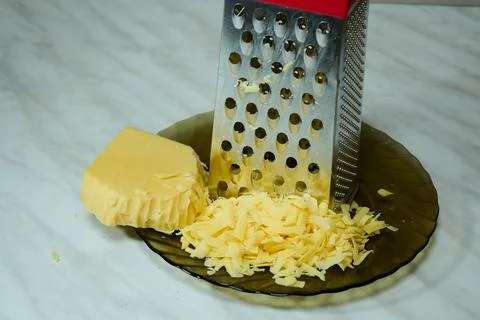 Grated Cheese on Red Grater in Kitchen Bowl Stock Photos
