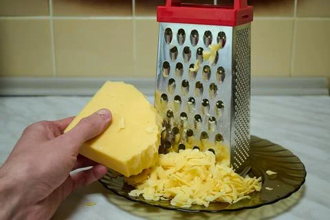 Grated Cheese on Red Grater in Kitchen Bowl Stock Photos