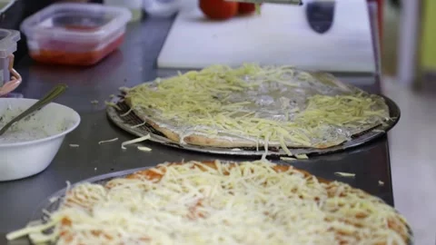 Grating cheese with a metal grater and pouring it over pizza crusts. Stock Footage 147273640