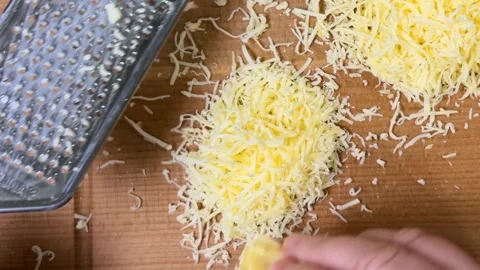 Grating hard cheese on a fine metal grater against a wooden board. Top view. Stock-Footage 301890747