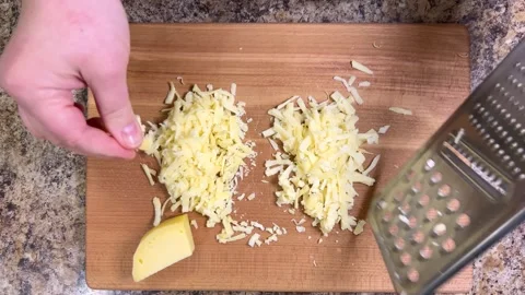 Grating hard cheese on a large metal grater against a wooden board. Top view. Stock Footage 300455873
