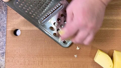 Grating hard cheese on a large metal grater against a wooden board. Top view. Video stock 301888396
