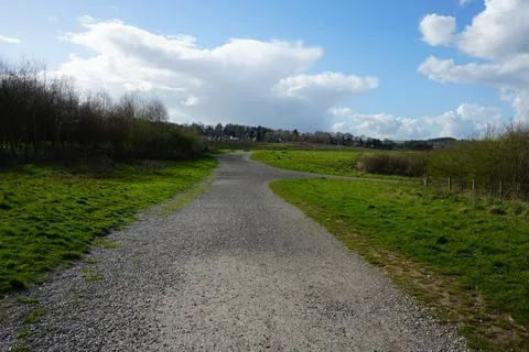 Gravel Path Through Green Fields Under Cloudy Sky With Village In North East Stockfoto's