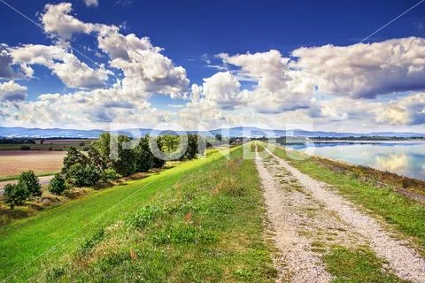 Gravel road along the shore of the lake with blue water Stock Photos