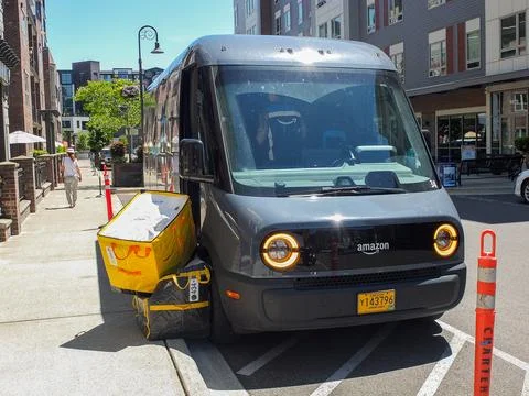Gray Amazon electric delivery van parked at the curb next to a yellow deliv.. Фото