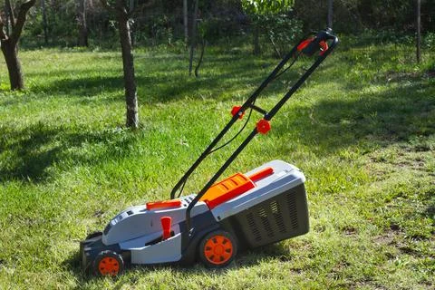 Gray and orange electrical mower on the grass in a sunny day Stock Photos
