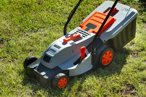 Gray and orange electrical mower on the grass in a sunny day Foto stock