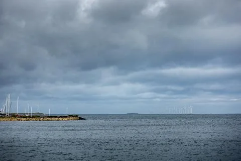 Gray and storm clouds overlooking a marina (left) and a distant wind farm Stock Photos