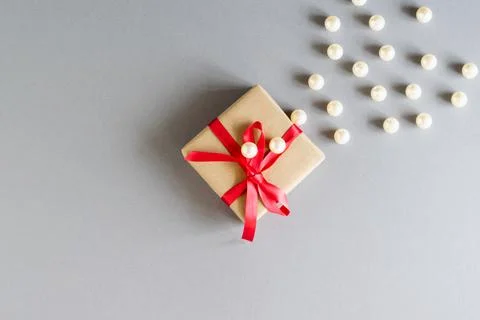 On a gray background, a gift in craft packaging with a red ribbon and white b Stock Photos