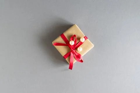 On a gray background, a gift in craft packaging with a red ribbon and white b Stock Photos