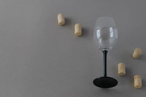 On a gray background, one empty glass wine goblet with scattered corks. Stock Photos