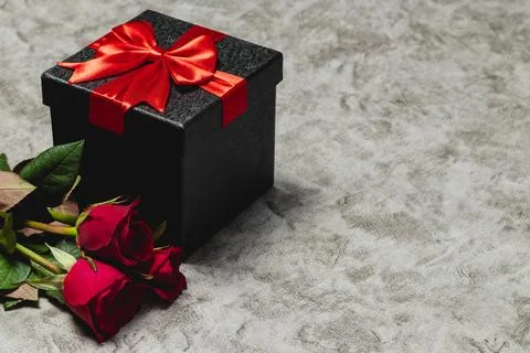 A gray background showcasing a gift box and a red rose. Stock Photos