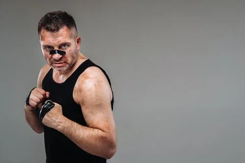 On a gray background stands a battered man in a black T shirt looking like a  Foto stock