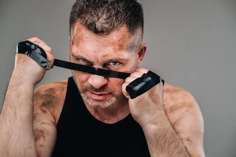 On a gray background stands a battered man in a black T shirt looking like a  Stock Photos