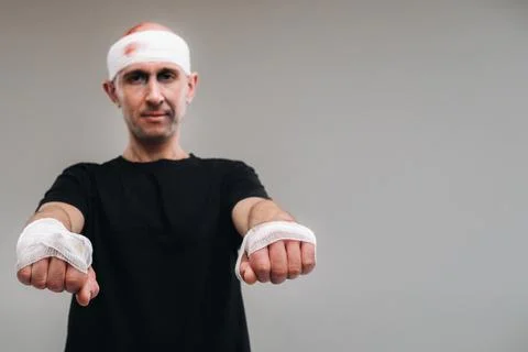 On a gray background stands a battered man in a black T-shirt With his hands  Foto stock