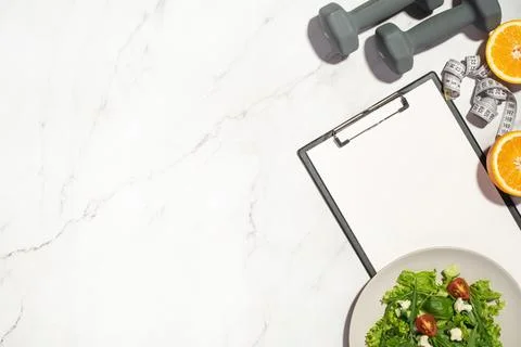 Gray background with tablet, lettuce, orange, dumbbells and measuring tape Stock Photos