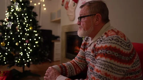 A gray-bearded elderly man with glasses and a knitted sweater sits alone by the Video stock 143863540