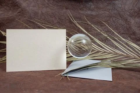 Gray blank postcard with a silver envelope, glass lens ball and a dried pal.. Stock Photos