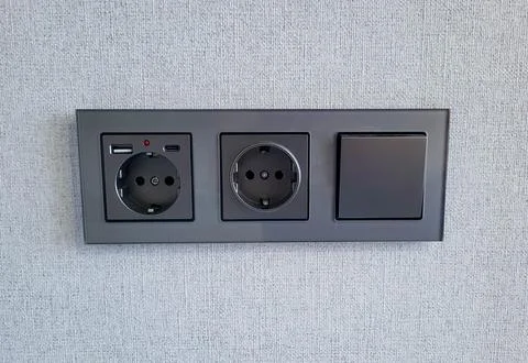 A gray block with a switch and sockets on a light colored wall. Stock Photos