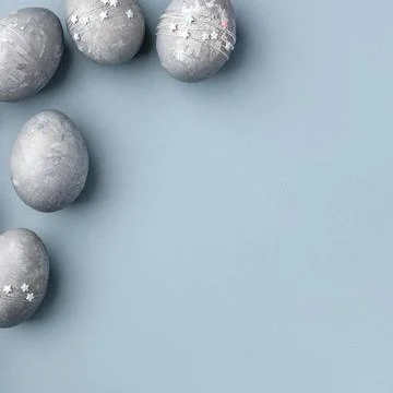 Gray-blue Easter eggs with stars on a blue table. Stock Photos