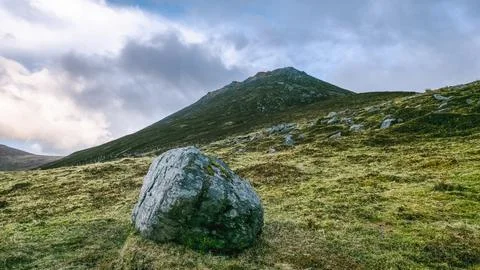 Gray boulder dominates the foreground, positioned on a grassy slope. Stock Photos