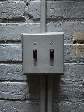 Gray brick wall with a rectangular electrical box with two black light swit.. Foto stock