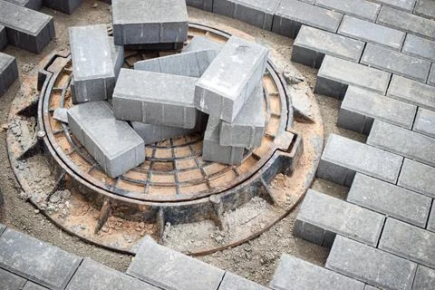Gray bricks are stacked around a manhole cover in an urban construction zone, Stock Photos