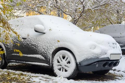 A gray car covered with the first snow against the background of yellow trees Stock Photos