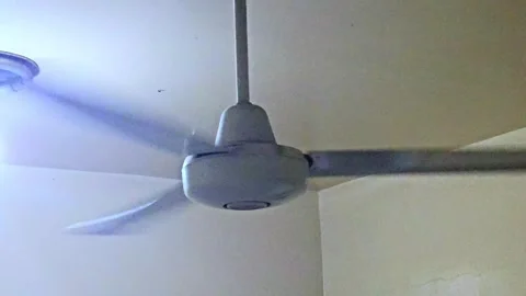 ​A gray ceiling fan is spinning rapidly in an indoor setting, creating a blur Video stock 322519358