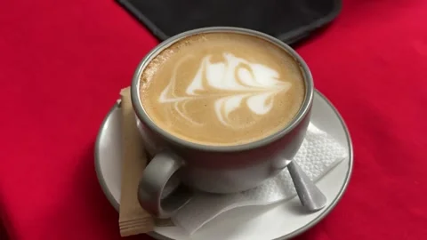 Gray ceramic mug of latte coffee with abstract foam art on red tablecloth cozy Stock Footage 345737662
