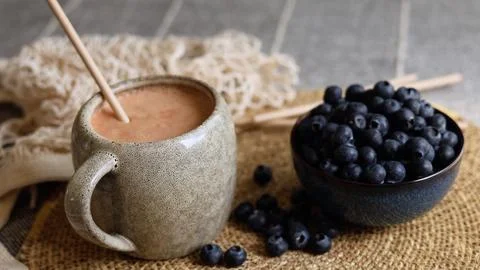 Gray ceramic mug with light brown smoothie sits beside dark blue bowl filled Stock Photos