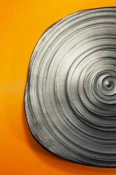 Gray ceramic plate with spiral texture on orange background Stock Photos