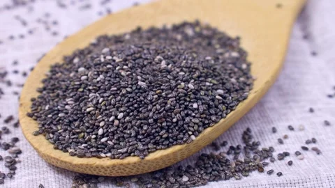 Gray chia seeds falling down into the wooden spoon close up Video stock 268850870
