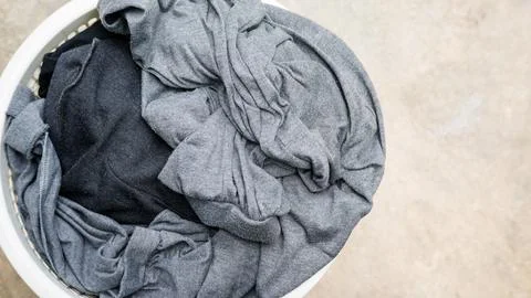 Gray clothes in a white hamper on a cement background. Stock Photos