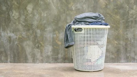Gray clothes in a white hamper on a cement background. Stock Photos