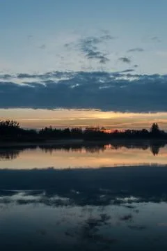 Gray cloud and trees on the shore reflecting in the water of the lake Stock Photos