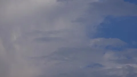 Gray clouds drifting slowly across a blue sky, opening and closing patches of su Stock Footage 340150284