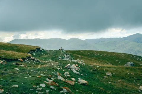 Gray clouds loom over green hills dotted with rocks Stock Photos