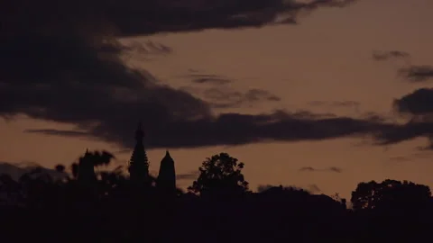 Gray clouds over silhouette of stupa and surrounding trees at dusk Stock Footage 139687183