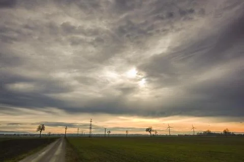 Gray clouds on the sky with sun in a flat landscape with windmills Stock Photos