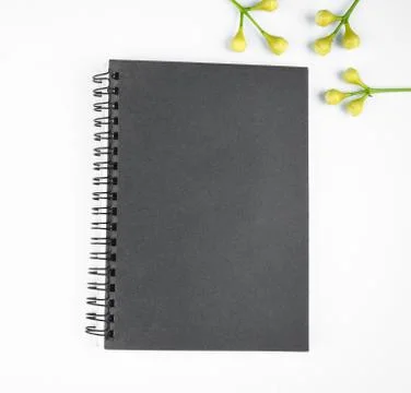 Gray colored paper diary and some small flowers before a white background Stock Photos