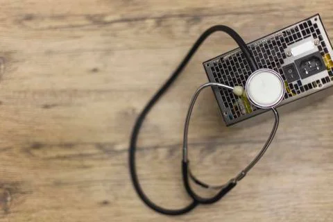 A gray computer power suply and phonendoscope on wooden board. Stock Photos