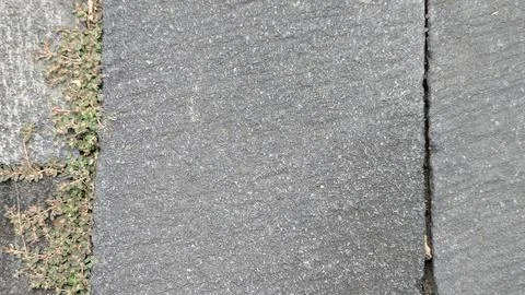 A gray concrete surface, divided into textured squares, has a small patch o.. 스톡 사진
