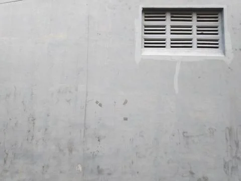 A gray concrete wall features a rectangular metal vent with horizontal slats, 스톡 사진